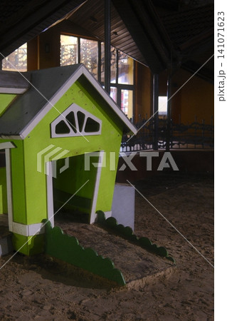 A bright green wooden playhouse with white trim sits on dark sand within an indoor play area A bright green wooden playhouse with white trim sits on dark sand within an indoor play area 141071623