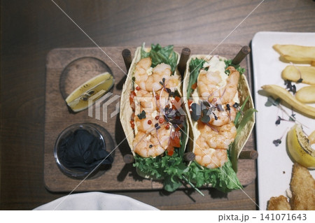 Two generously filled shrimp tacos sit on a wooden serving board with a lime wedge Two generously filled shrimp tacos sit on a wooden serving board with a lime wedge 141071643