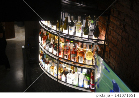 Dark bar: backlit bottles, sleek curved bar, brick wall, TV playing a game Dark bar: backlit bottles, sleek curved bar, brick wall, TV playing a game 141071651