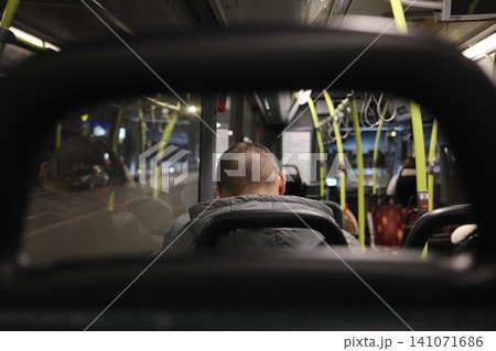 Nighttime travel inside a public transport bus with a person sitting from the back on an evening commute Nighttime travel inside a public transport bus with a person sitting from the back on an evening commute 141071686