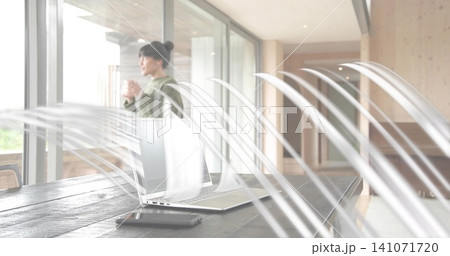 Holding mug, woman in green sweater gazing through glass doors at home, laptop visible, copy space Holding mug, woman in green sweater gazing through glass doors at home, laptop visible, copy space 141071720