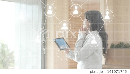 Holding woman wearing light gray sweater touching chin while viewing tablet near glass door overlay Holding woman wearing light gray sweater touching chin while viewing tablet near glass door overlay 141071746