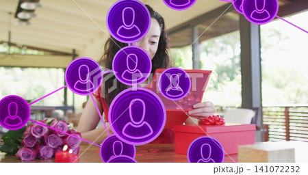 Opening adult woman in red dress reading card, holding gift at wooden patio table, purple overlays 141072232