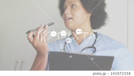 Speaking nurse in blue scrubs holding phone to mouth and clipboard in clinic, wearing stethoscope 141072338