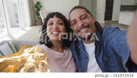 Taking couple wearing light pink T-shirt and blue denim shirt on sofa at home, holding smartphone Taking couple wearing light pink T-shirt and blue denim shirt on sofa at home, holding smartphone 141072414