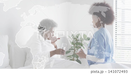 Offering caregiver in scrubs handing pill while senior sipping water at bedside, map overlay 141072493