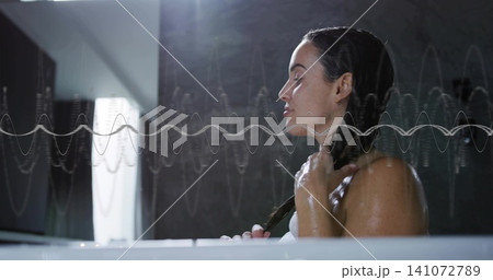 Holding wet braid, adult woman in towel sitting in bathtub near window with waveform, copy space 141072789