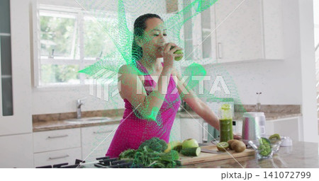 Sipping woman in sleeveless magenta top at kitchen island tasting green smoothie with halved kiwi Sipping woman in sleeveless magenta top at kitchen island tasting green smoothie with halved kiwi 141072799