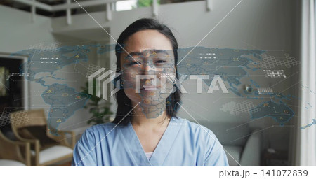 Standing Asian woman wearing light blue scrubs in home loft, AR world map overlaying chest 141072839
