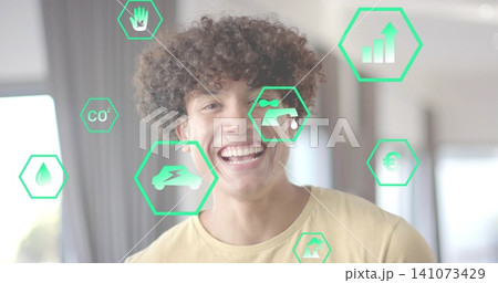 Smiling man wearing yellow tee at home, displaying green hex icons with eco and finance symbols Smiling man wearing yellow tee at home, displaying green hex icons with eco and finance symbols 141073429