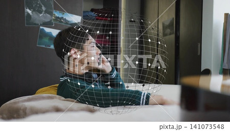 Reclining teen in green sweater holding phone to ear with headset on bed, AR globe overlay Reclining teen in green sweater holding phone to ear with headset on bed, AR globe overlay 141073548