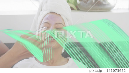 Reclining client receiving purple facial mask at spa, with towel turban, eye pads and tech hand 141073632