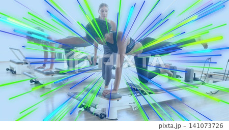 Performing female participant extending single leg on reformer at pilates studio, in dark leggings Performing female participant extending single leg on reformer at pilates studio, in dark leggings 141073726