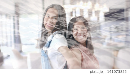 Standing back-to-back woman and teen smiling in bright room, wearing overalls, pink top, overlay 141073833