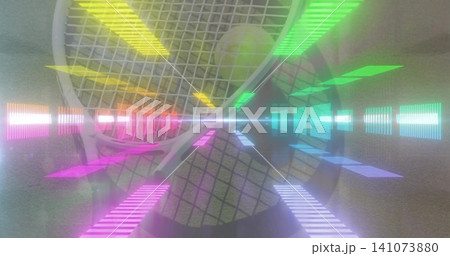Lying white tennis racket showing strings with yellow ball on gray mat, casting colorful neon flare Lying white tennis racket showing strings with yellow ball on gray mat, casting colorful neon flare 141073880