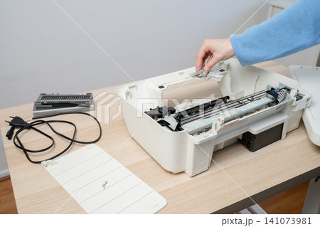 Woman Cleaning and Servicing a Disassembled Home Inkjet Printer on Wooden Desk Woman Cleaning and Servicing a Disassembled Home Inkjet Printer on Wooden Desk 141073981