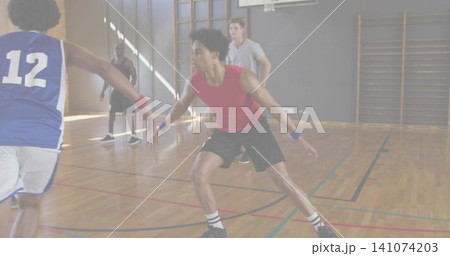 Defending man in red sleeveless shirt holding low stance on school gym hardwood floor, with hoop Defending man in red sleeveless shirt holding low stance on school gym hardwood floor, with hoop 141074203