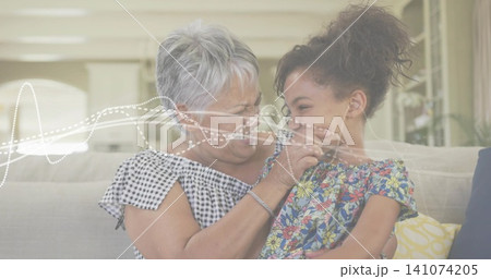 Smiling grandma and granddaughter laughing on home sofa, gingham top floral dress waveform overlay Smiling grandma and granddaughter laughing on home sofa, gingham top floral dress waveform overlay 141074205