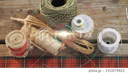 Displaying large twine ball on worn tabletop, red-striped jute, metallic spools, tartan, ring flare 141074922
