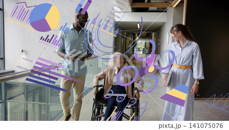 Walking staff guiding woman in wheelchair wearing blazer down care hall, with tablet, notebook AR 141075076