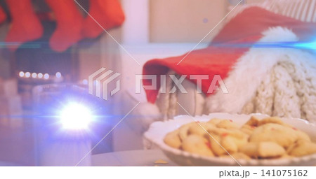 Displaying white scalloped bowl holding cookies on tabletop front, with candle flare and Santa hat Displaying white scalloped bowl holding cookies on tabletop front, with candle flare and Santa hat 141075162