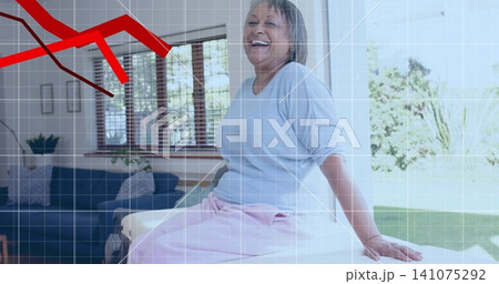 Smiling senior woman sitting on seat in sunny living room, in light-blue top, red graph overlay Smiling senior woman sitting on seat in sunny living room, in light-blue top, red graph overlay 141075292