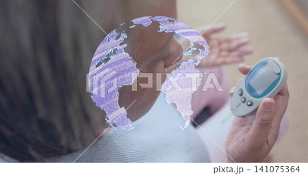 Holding glucometer, senior woman wearing blue sweater checking glucose at home, with hologram globe Holding glucometer, senior woman wearing blue sweater checking glucose at home, with hologram globe 141075364