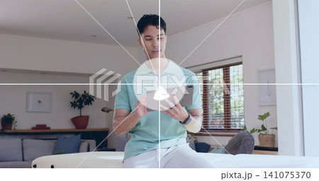 Sitting man wearing mint polo, gray pants and smartwatch on ottoman at home, holding tablet 141075370