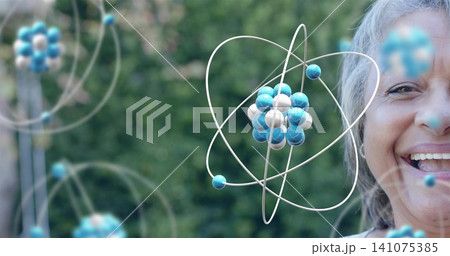 Smiling senior woman wearing light top, posing in garden with floating atom models, copy space Smiling senior woman wearing light top, posing in garden with floating atom models, copy space 141075385