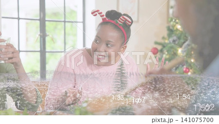 Smiling woman in pink sweater and candy-cane headband talking at living room table, numeric overlay Smiling woman in pink sweater and candy-cane headband talking at living room table, numeric overlay 141075700