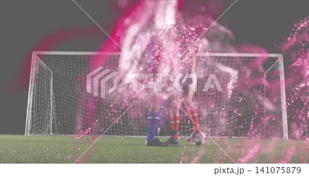 Competing two soccer players vying for ball on grass pitch at night, with goal, pink-smoke, cleats 141075879