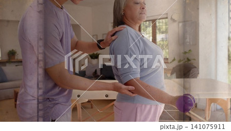 Helping senior woman in blue top and pink pants holding purple ball at home, man supporting Helping senior woman in blue top and pink pants holding purple ball at home, man supporting 141075911