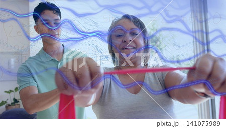 Stretching senior woman in grey tee pulling red resistance band at home helper guiding blue overlay 141075989