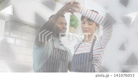 Raising joined hands, couple wearing striped aprons celebrating at home kitchen counter with plant 141076053