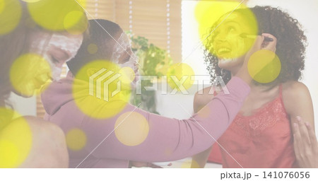 Applying eye makeup center woman using mascara on right friend at home in sleepwear, with masks Applying eye makeup center woman using mascara on right friend at home in sleepwear, with masks 141076056
