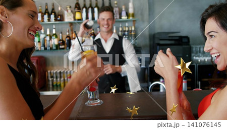 Laughing women at bar wearing dark and red dresses holding cocktails, bartender shaking shaker Laughing women at bar wearing dark and red dresses holding cocktails, bartender shaking shaker 141076145