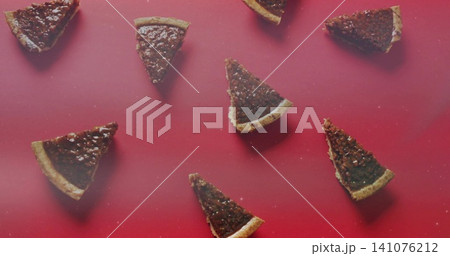 Arranging triangular nutty tart slices on red tabletop showing pastry crusts, nut pieces and crumbs Arranging triangular nutty tart slices on red tabletop showing pastry crusts, nut pieces and crumbs 141076212