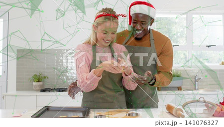 Baking couple wearing gray aprons and Santa hat shaping cookies at marble counter, with cutters Baking couple wearing gray aprons and Santa hat shaping cookies at marble counter, with cutters 141076327