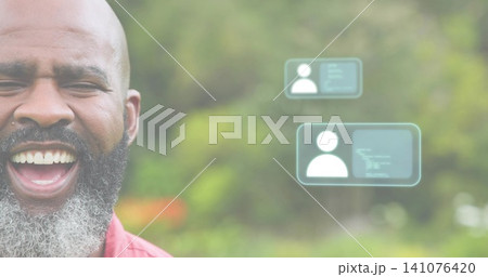 Laughing man with salt-pepper beard wearing red collared shirt in park, with UI cards, copy space 141076420