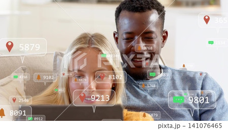 Sitting couple viewing laptop in living room man blue sweater woman light top digital overlays Sitting couple viewing laptop in living room man blue sweater woman light top digital overlays 141076465
