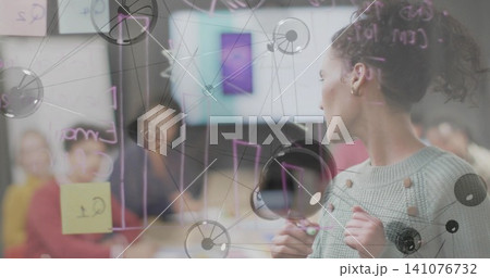Leading woman with bun wearing sweater noting charts on glass with marker sticky notes, copy space 141076732