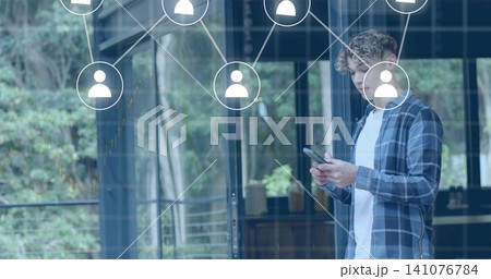 Holding smartphone, man in blue plaid shirt viewing network icons on glass doors, copy space 141076784