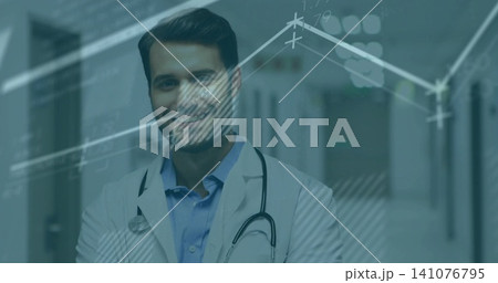 Standing male doctor wearing white lab coat and stethoscope in hospital hallway showing data charts 141076795