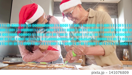 Decorating couple in Santa hats leaning over kitchen with binary band, piping red and green icing Decorating couple in Santa hats leaning over kitchen with binary band, piping red and green icing 141076809