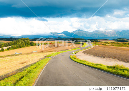 夏の終わりの北海道美瑛町の丘の上から見た十勝岳連峰と先に続く道 141077171