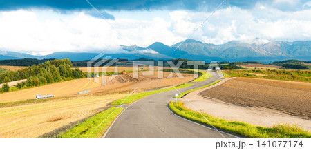 夏の終わりの北海道美瑛町の丘の上から見た十勝岳連峰と先に続く道 夏の終わりの北海道美瑛町の丘の上から見た十勝岳連峰と先に続く道 141077174