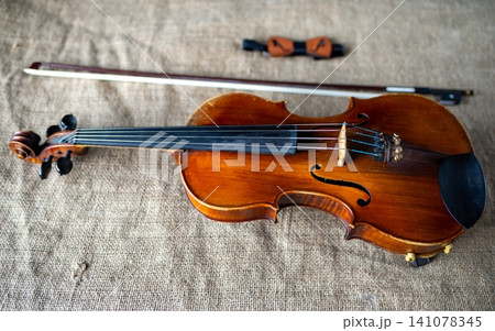 Classic wooden violin with bow and wooden bow tie on burlap Classic wooden violin with bow and wooden bow tie on burlap 141078345
