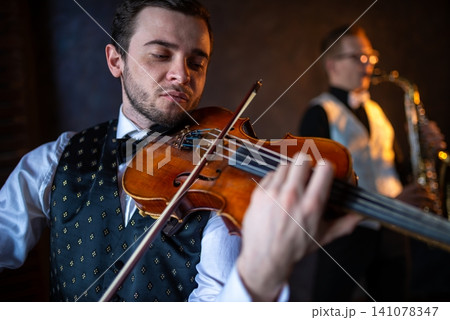 Close up of a violinist playing with a saxophonist out of focus Close up of a violinist playing with a saxophonist out of focus 141078347