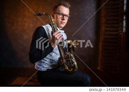 Young man with glasses sitting with golden saxophone Young man with glasses sitting with golden saxophone 141078349