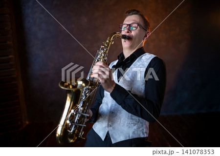 Young man in glasses playing golden saxophone 141078353